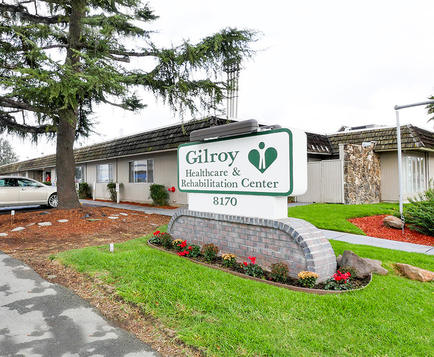 The front of the Gilroy Care facility, green grass, trees, and monument sign