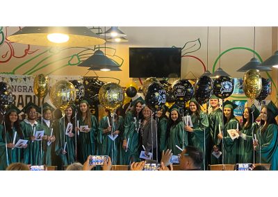 Balloons and decorations and several graduates wearing green gowns and hats at Clinitrack graduation