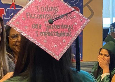 A graduate wearing green gown and hat saying "Today's accomplishments are yesterday's impossibilities" at Clinitrack graduation