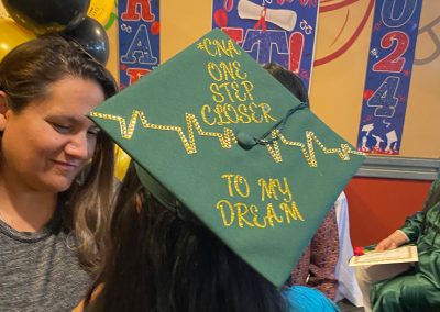 A graduate wearing green gown and hat saying "CNA One step closer to my dream" at Clinitrack graduation